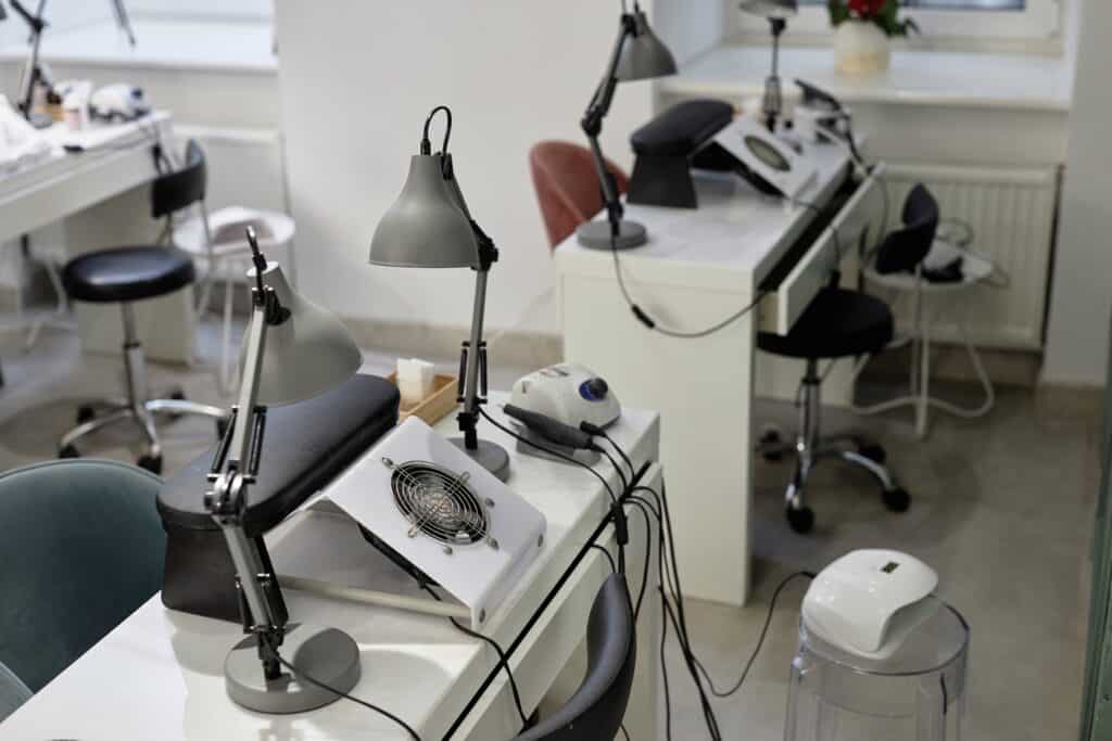 NYCOSH - A clean, modern nail salon with empty workstations, each equipped with task lamps, nail dryers, stools, and manicure tools.