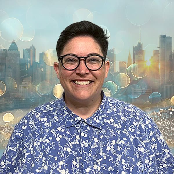 NYCOSH - Person with short dark hair and glasses, smiling, wearing a blue floral shirt, with a city skyline and bright light effects in the background.