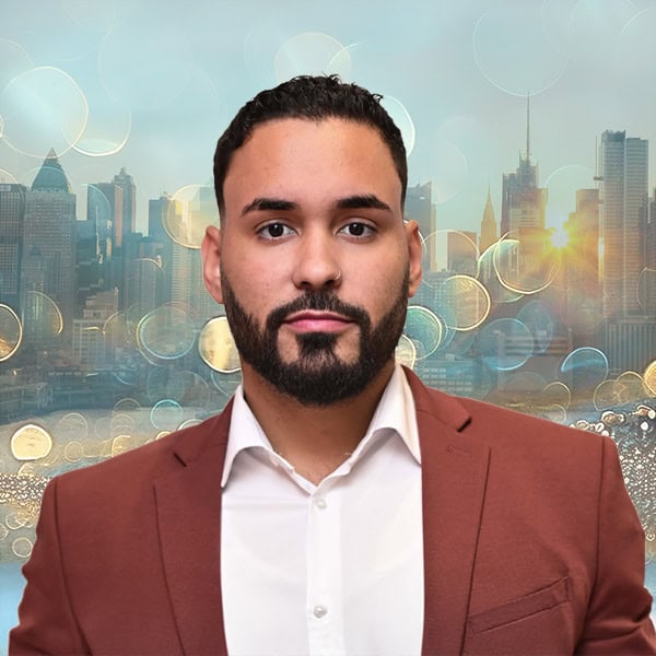 NYCOSH - A man in a white shirt and brown blazer stands in front of a city skyline with sunlight and bokeh light effects in the background.