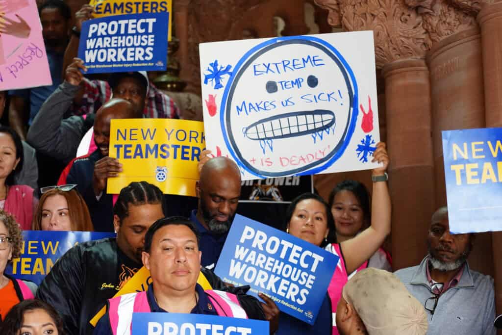 NYCOSH - A group of people from the Temp Coalition hold signs reading "PROTECT WAREHOUSE WORKERS" and display a poster warning about extreme temperatures making workers sick.