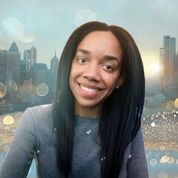 NYCOSH - Woman with long straight black hair and a gray top smiles at the camera, with a city skyline and soft light bokeh in the background.