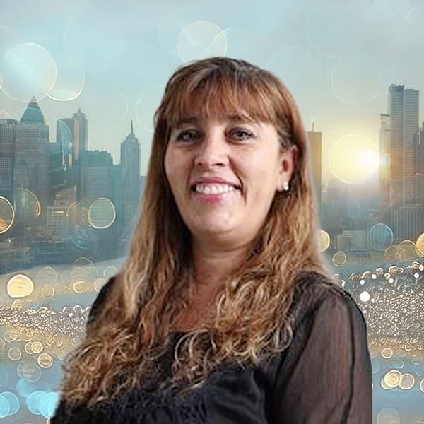 NYCOSH - A woman with long brown hair and a black top smiles in front of a city skyline with bokeh light effects.