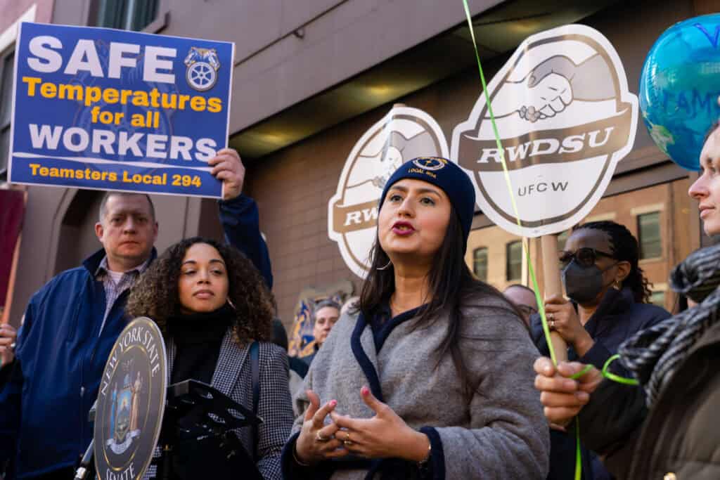 NYCOSH - A group of people at a rally, organized by the Temp Coalition, hold signs advocating for safe workplace temperatures; one woman speaks to the crowd.
