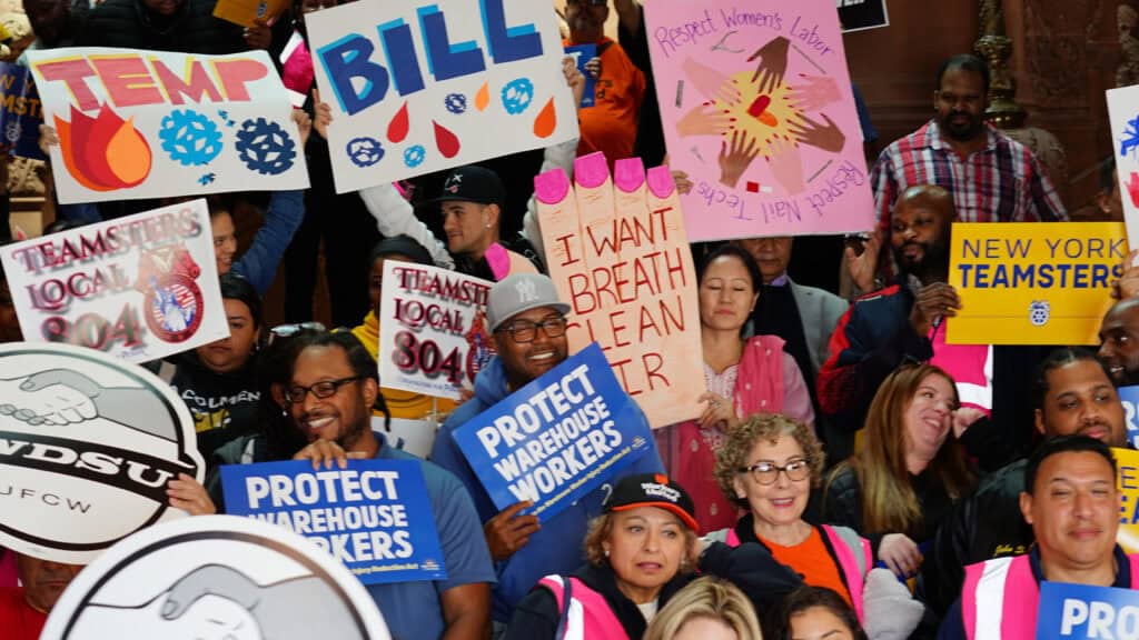NYCOSH - A group of people hold signs supporting warehouse workers, labor unions, and respect for women's labor at a rally protesting wage theft.