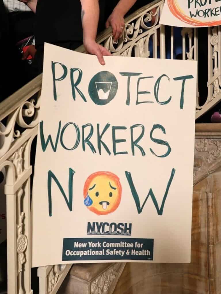 NYCOSH - A person holds a sign on a staircase reading “Protect Workers Now” with a crying emoji, and “NYCOSH New York Committee for Occupational Safety & Health” at the bottom.